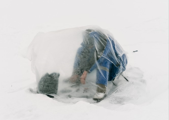 Ice fisherman covers himself in a plastic bag to shield from the weather